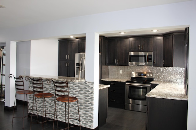 kitchen with appliances with stainless steel finishes, tasteful backsplash, a kitchen breakfast bar, light stone countertops, and recessed lighting