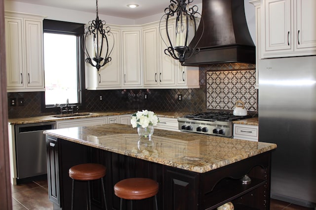 kitchen with appliances with stainless steel finishes, a sink, premium range hood, a kitchen island, and light stone countertops