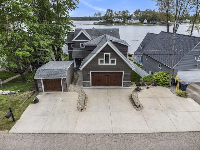 view of front of house featuring driveway, a water view, a storage shed, stone siding, and a garage