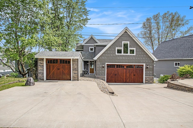 view of front facade with stone siding, concrete driveway, roof with shingles, and a garage
