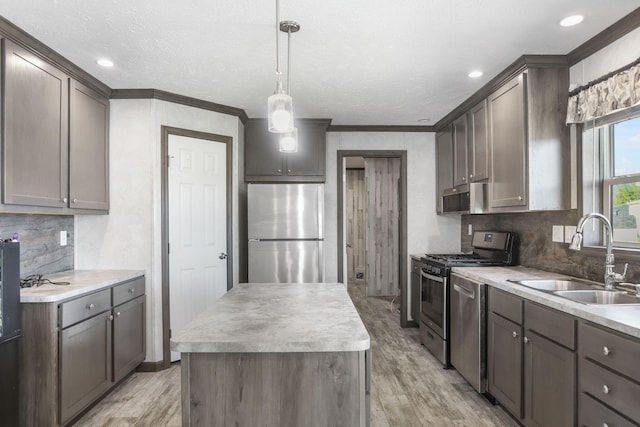 kitchen with stainless steel appliances, a sink, light wood-style flooring, a center island, and crown molding