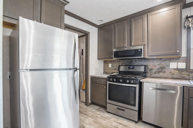 kitchen featuring appliances with stainless steel finishes, light countertops, light wood-type flooring, ornamental molding, and tasteful backsplash