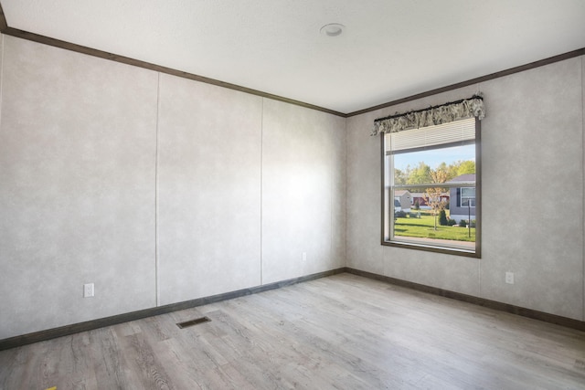 empty room with wood finished floors, crown molding, and baseboards
