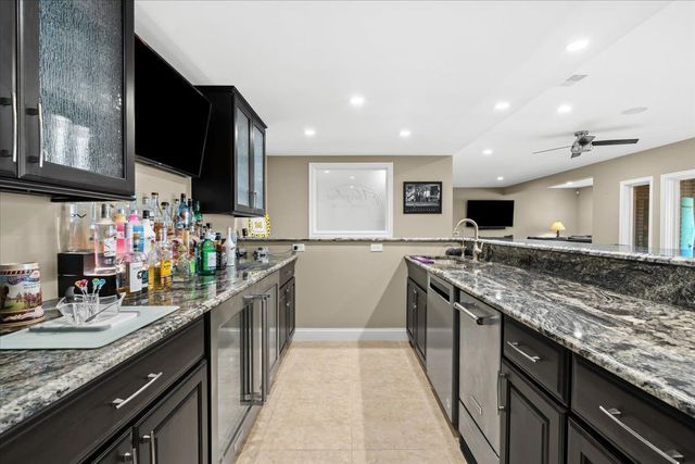 8353 Pier Point Ct, South Lyon, MI 48178 - kitchen with a sink, baseboards, recessed lighting, stone countertops, and glass insert cabinets