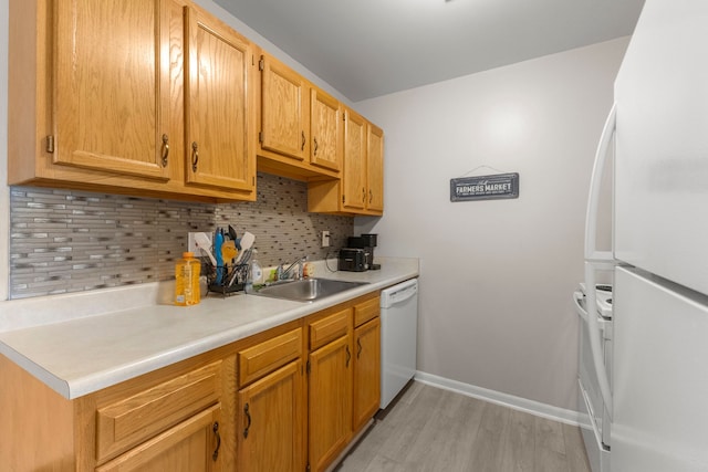 kitchen with white appliances, a sink, tasteful backsplash, light wood-style flooring, and light countertops
