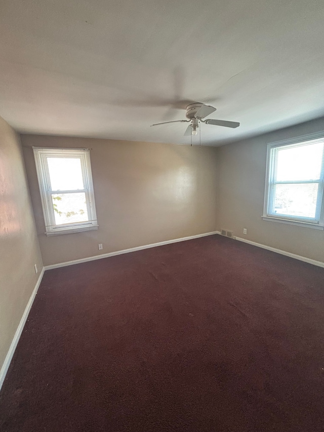 unfurnished room with plenty of natural light, baseboards, and dark colored carpet