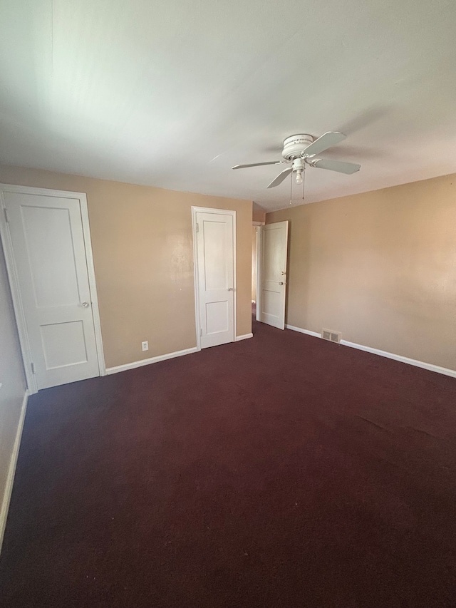 empty room with baseboards, ceiling fan, and dark colored carpet