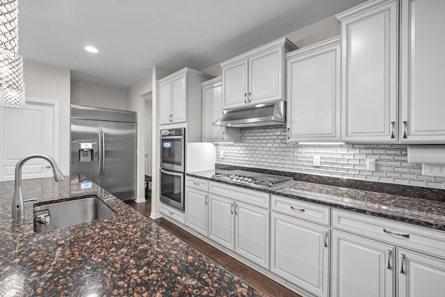 kitchen featuring appliances with stainless steel finishes, a sink, under cabinet range hood, white cabinets, and tasteful backsplash