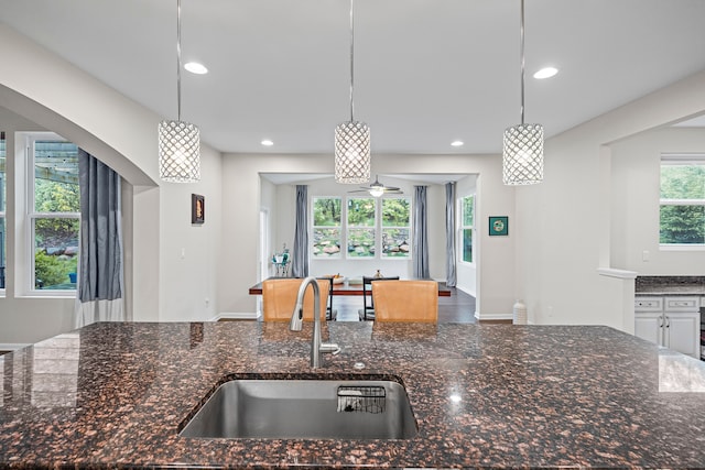 kitchen with a sink, hanging light fixtures, dark stone countertops, recessed lighting, and a ceiling fan