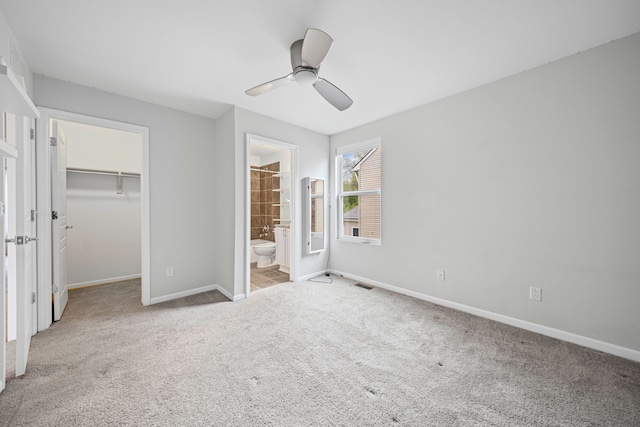 unfurnished bedroom with carpet flooring, a spacious closet, baseboards, a closet, and ceiling fan