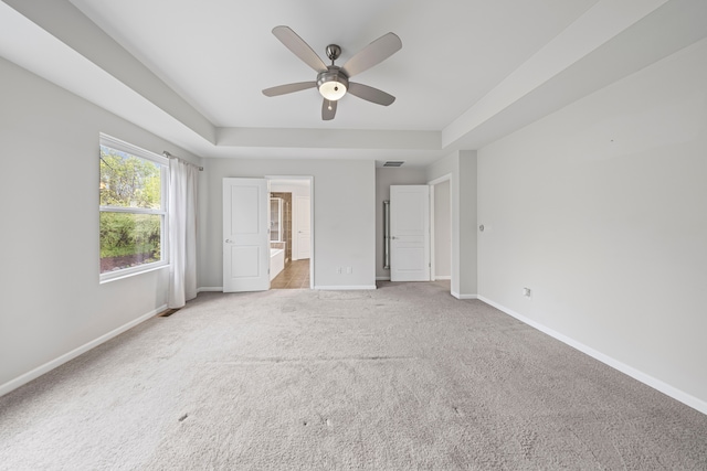unfurnished bedroom with light carpet, baseboards, and a raised ceiling
