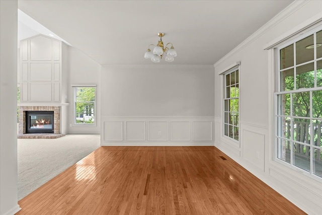 unfurnished dining area with a chandelier, wood finished floors, crown molding, wainscoting, and a fireplace