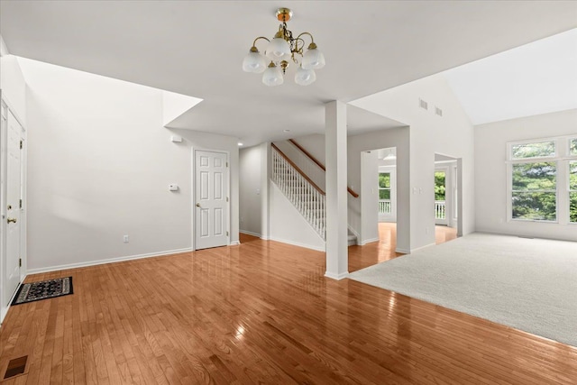 unfurnished living room with stairway, wood finished floors, a chandelier, vaulted ceiling, and baseboards
