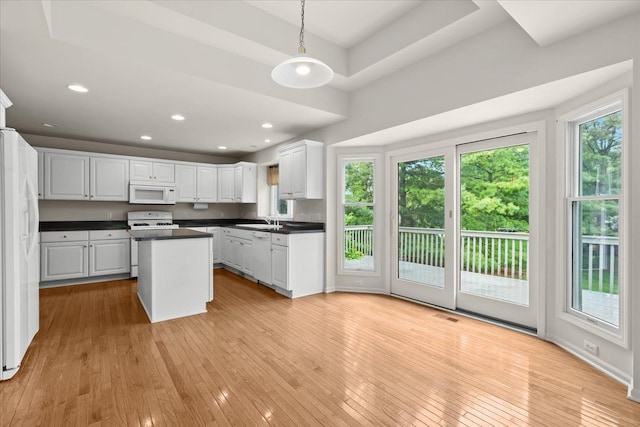 kitchen with white appliances, a sink, light wood-style flooring, dark countertops, and a kitchen island