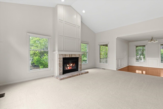 unfurnished living room with carpet, high vaulted ceiling, a chandelier, a brick fireplace, and plenty of natural light