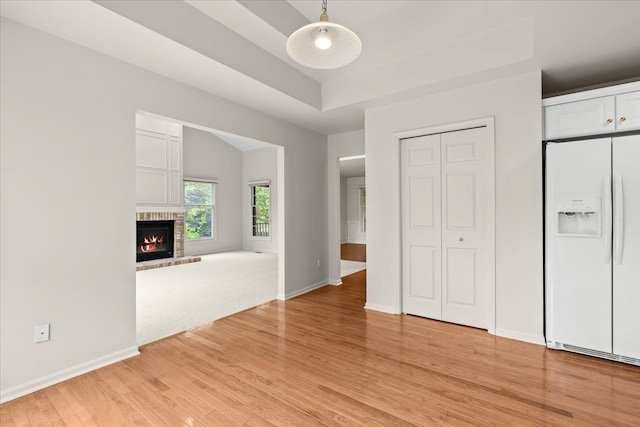 unfurnished living room with light wood-type flooring, baseboards, a brick fireplace, and a raised ceiling