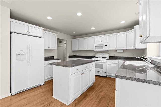 kitchen with white appliances, a sink, a kitchen island, white cabinets, and light wood finished floors