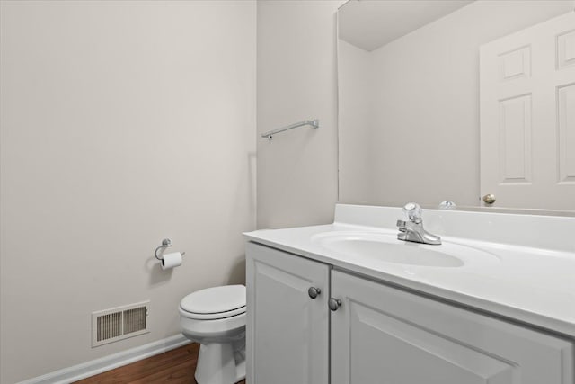 bathroom with toilet, vanity, wood finished floors, and baseboards