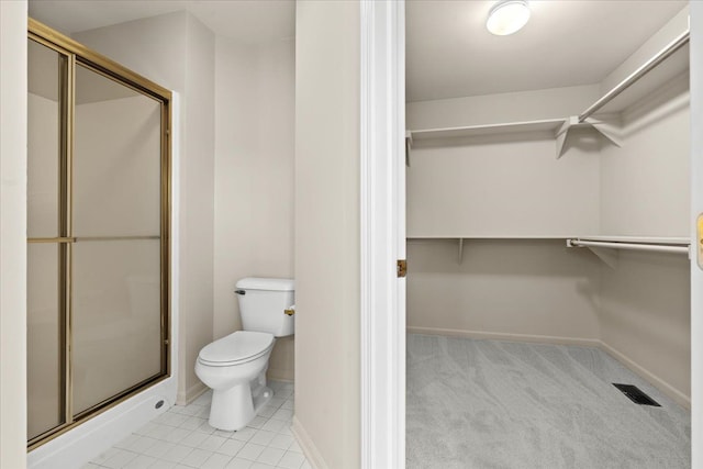 full bath with toilet, a stall shower, a spacious closet, baseboards, and tile patterned flooring