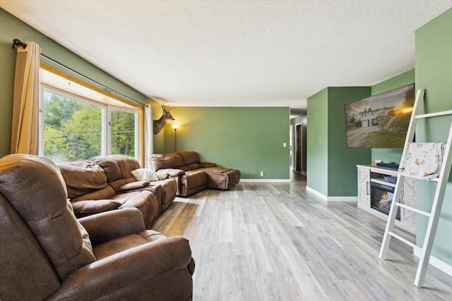 living area with wood finished floors, a textured ceiling, a glass covered fireplace, and baseboards