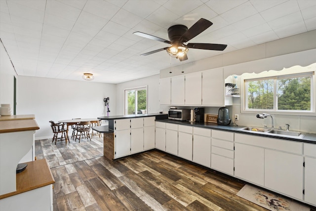 kitchen with a sink, stainless steel microwave, a peninsula, and dark wood-type flooring