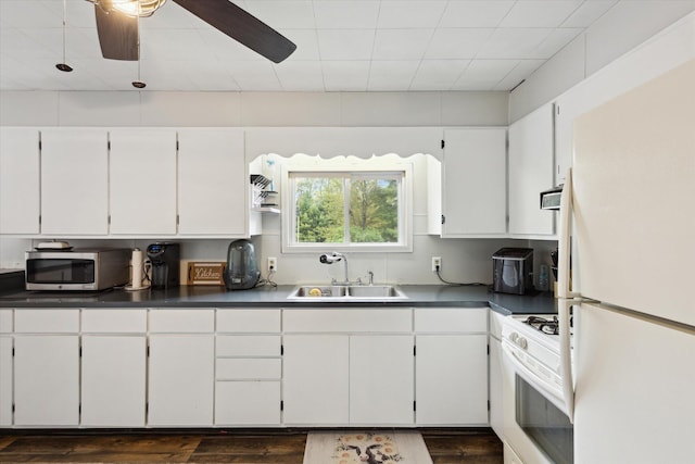 kitchen with white appliances, a sink, dark wood-style flooring, dark countertops, and white cabinets