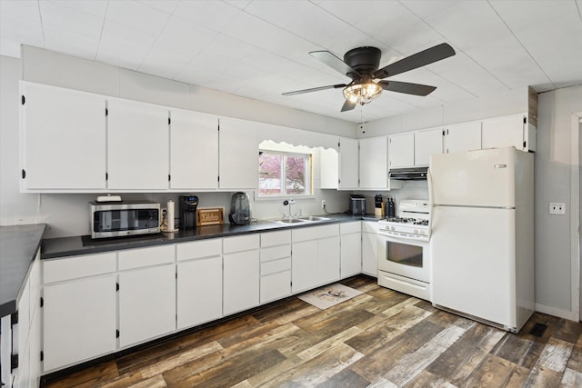 kitchen with white appliances, a sink, a ceiling fan, dark countertops, and dark wood-type flooring