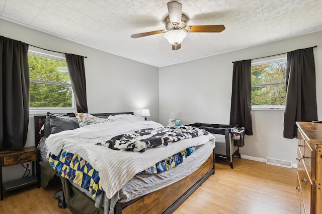 bedroom with multiple windows, light wood-style flooring, ceiling fan, and baseboards