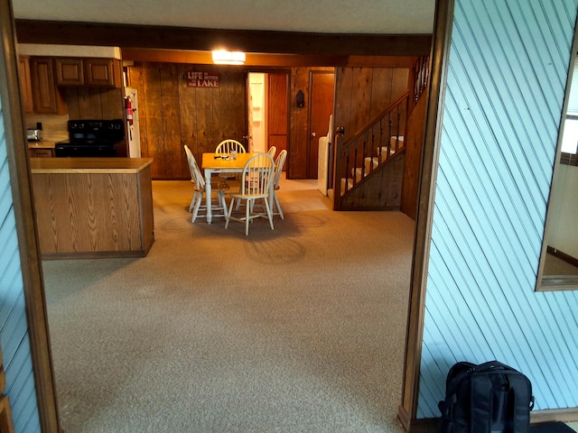 dining area with light carpet, wood walls, and stairway