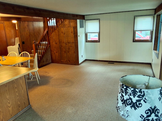 carpeted living room with stairway, wooden walls, and baseboards