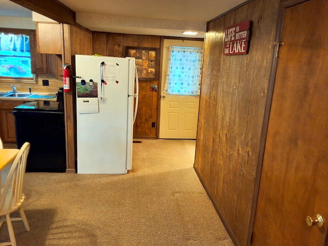 kitchen with freestanding refrigerator, wooden walls, light carpet, a sink, and range with electric cooktop