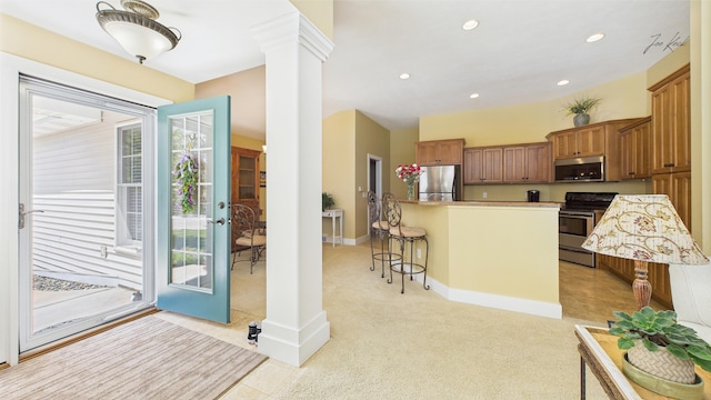 kitchen with stainless steel appliances, ornate columns, a breakfast bar area, brown cabinetry, and light colored carpet