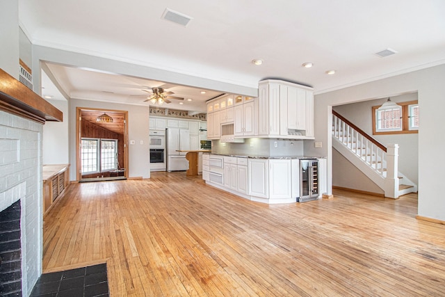 kitchen with freestanding refrigerator, wine cooler, a fireplace, light wood finished floors, and white cabinetry