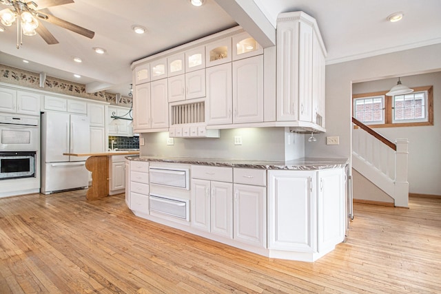 kitchen with white appliances, a warming drawer, light wood finished floors, white cabinets, and recessed lighting