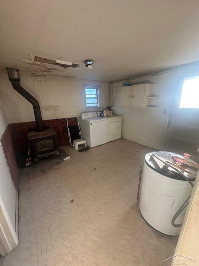 basement with a wood stove, light floors, and washer and clothes dryer