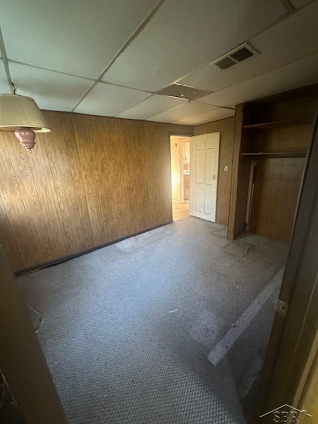 unfurnished bedroom featuring wooden walls, carpet, a closet, and a paneled ceiling
