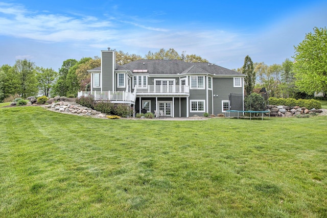 rear view of house featuring french doors, a trampoline, a wooden deck, a chimney, and a lawn
