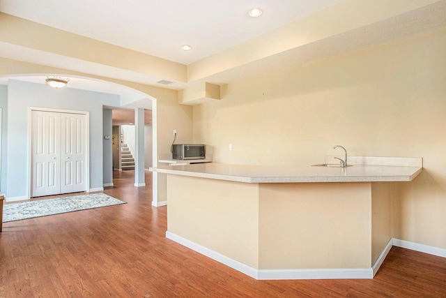 kitchen featuring stainless steel microwave, arched walkways, baseboards, a peninsula, and light countertops