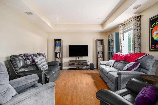 living area with light wood finished floors, a tray ceiling, baseboards, and recessed lighting