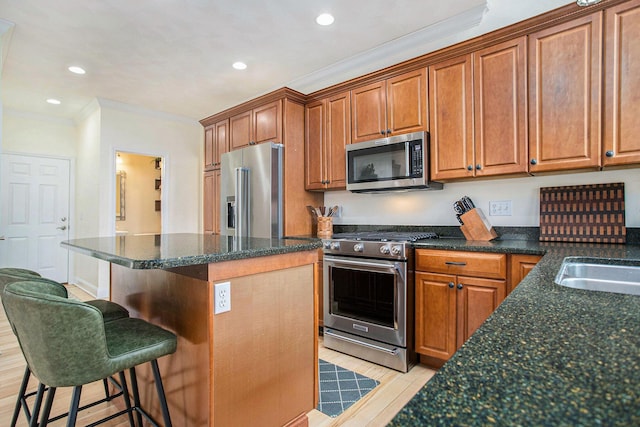 kitchen featuring appliances with stainless steel finishes, crown molding, a kitchen bar, brown cabinetry, and a kitchen island