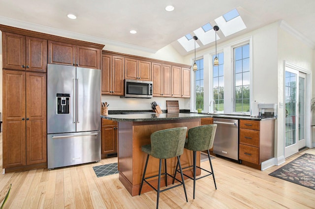kitchen with appliances with stainless steel finishes, a skylight, a sink, light wood finished floors, and ornamental molding