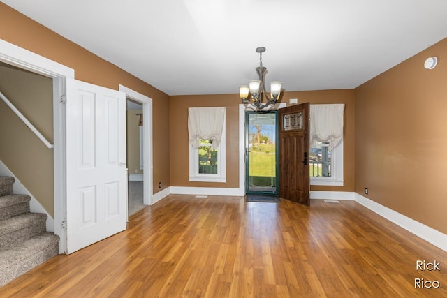unfurnished dining area featuring a chandelier, stairway, light wood-style floors, and baseboards