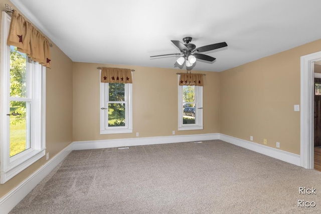 carpeted empty room with plenty of natural light, a ceiling fan, and baseboards