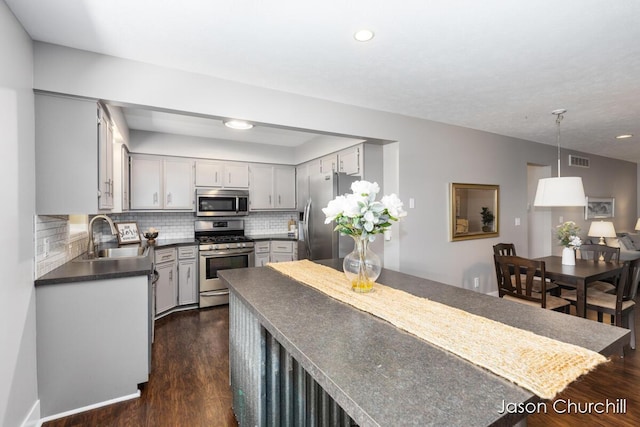 kitchen featuring stainless steel appliances, a sink, dark countertops, dark wood finished floors, and tasteful backsplash