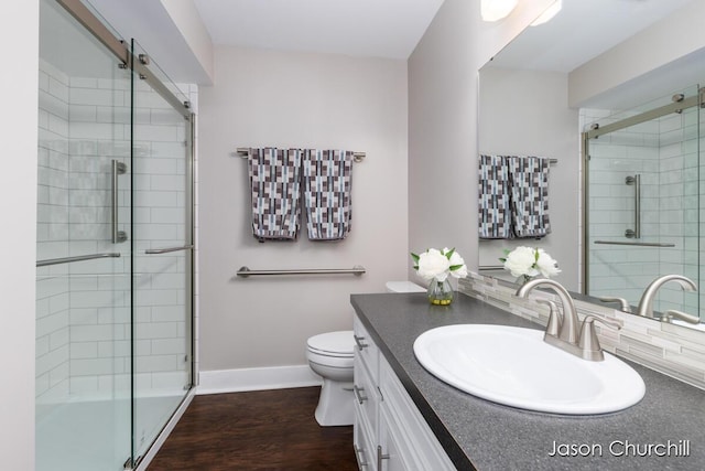 bathroom with a stall shower, toilet, vanity, baseboards, and wood finished floors