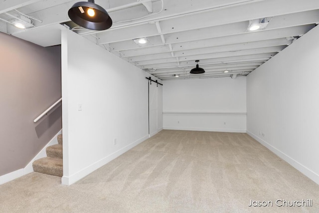 finished below grade area with light colored carpet, baseboards, a barn door, and stairs
