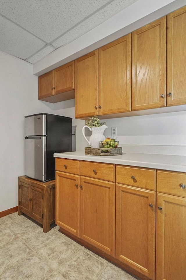 kitchen with freestanding refrigerator, light countertops, baseboards, brown cabinets, and a paneled ceiling