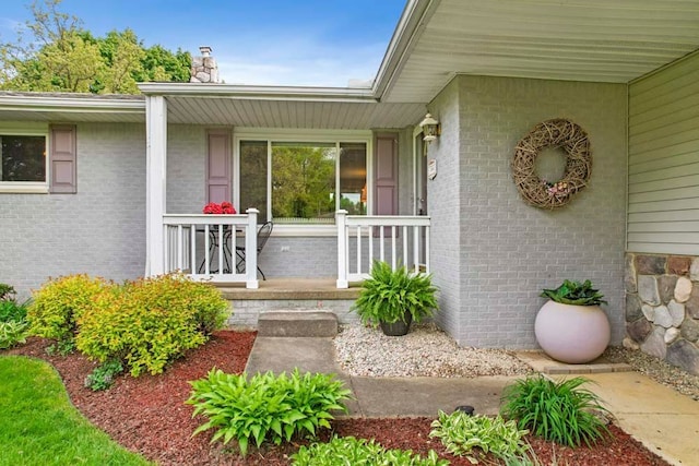 property entrance with a porch, a chimney, and brick siding