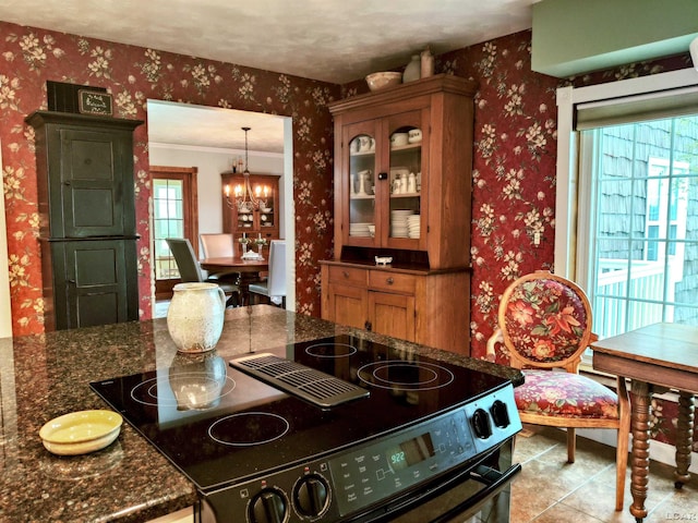 kitchen with black range with electric stovetop, wallpapered walls, a chandelier, tile patterned flooring, and brown cabinetry
