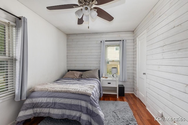 bedroom featuring wooden walls, wood finished floors, and a ceiling fan
